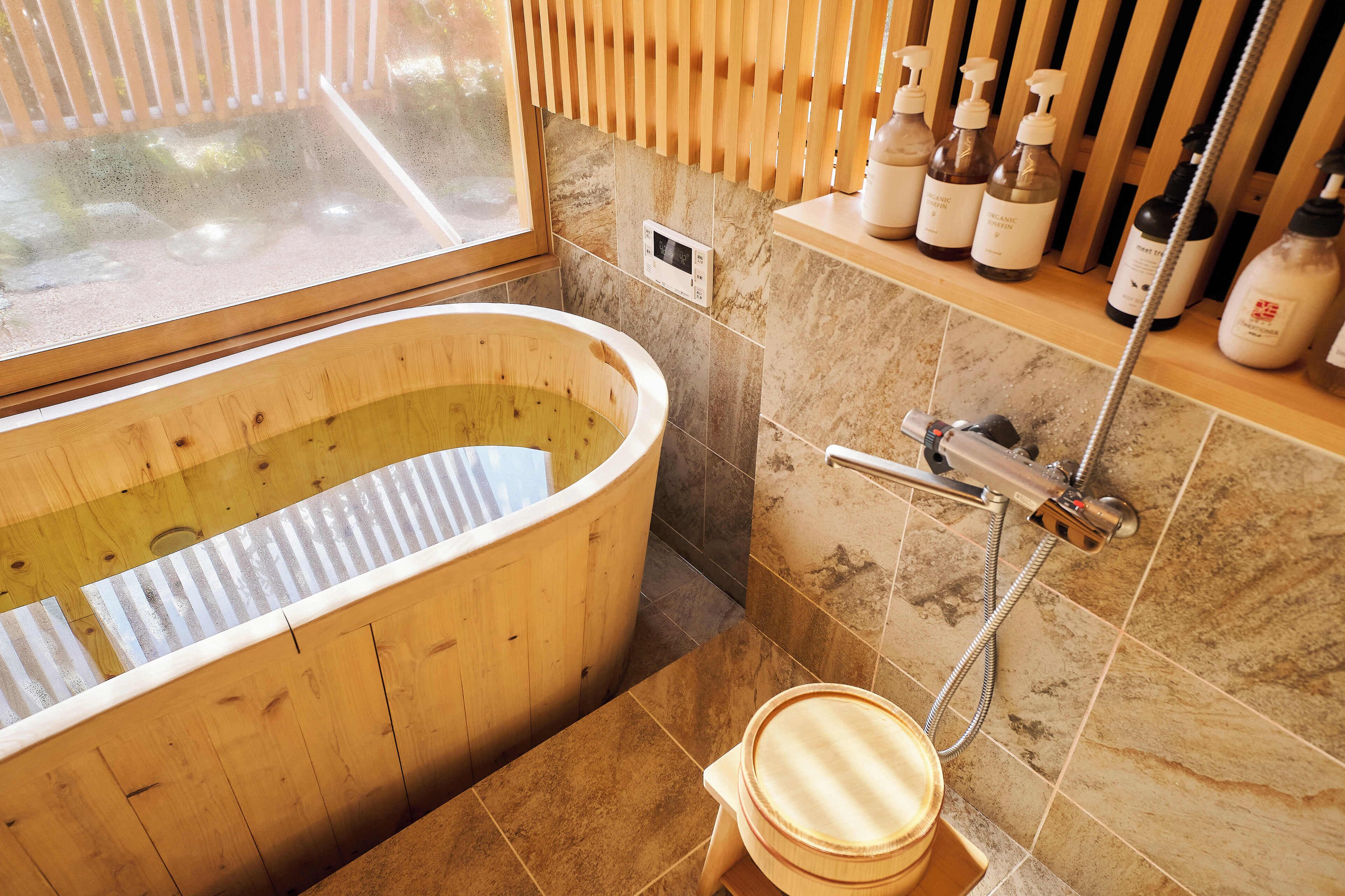 A wooden bathtub, a toilet, a shower, and a shelf with toiletries.
