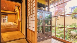 Una habitación japonesa tradicional con suelo de tatami, una cama de madera baja, puertas correderas shoji y vista a un jardín por un gran ventanal.