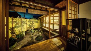 Um quarto japonês tradicional com tatames, um painel shoji e uma pequena área de jardim com pedras e plantas.