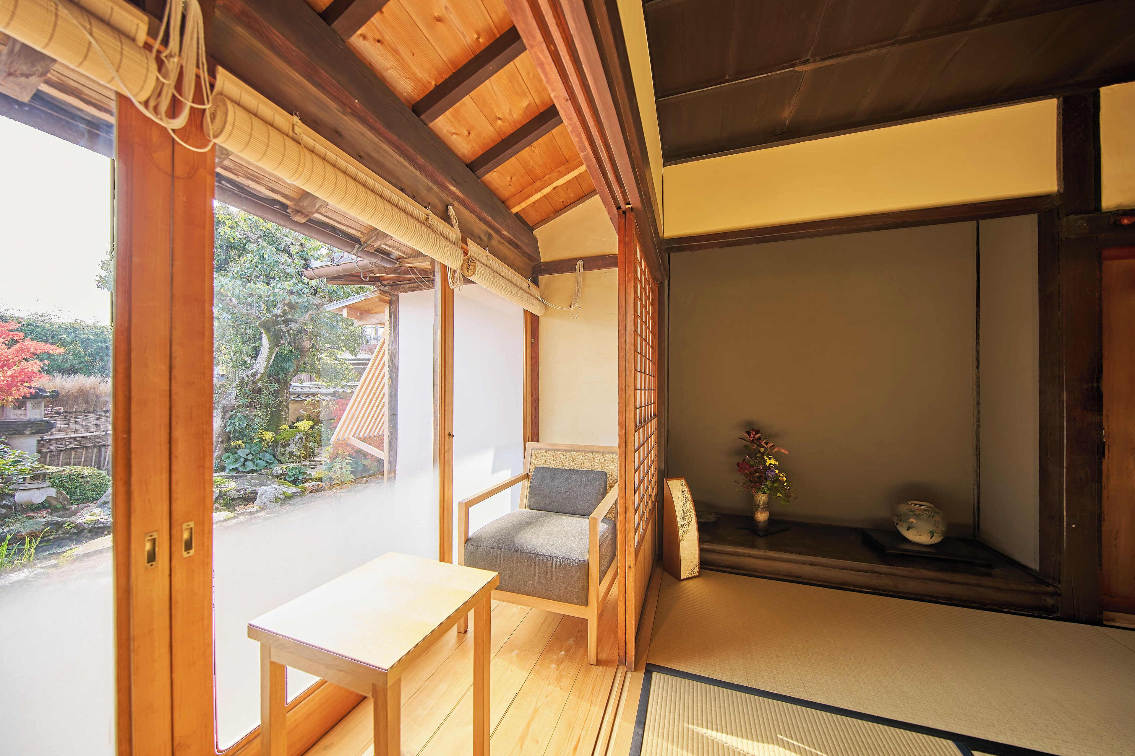 Una habitación japonesa tradicional con suelo de tatami, una mesa de madera baja, una silla acolchada y un puertas correderas que dan a un jardín.