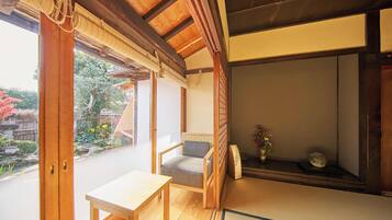Una habitación japonesa tradicional con suelo de tatami, una mesa de madera baja, una silla acolchada y un puertas correderas que dan a un jardín.