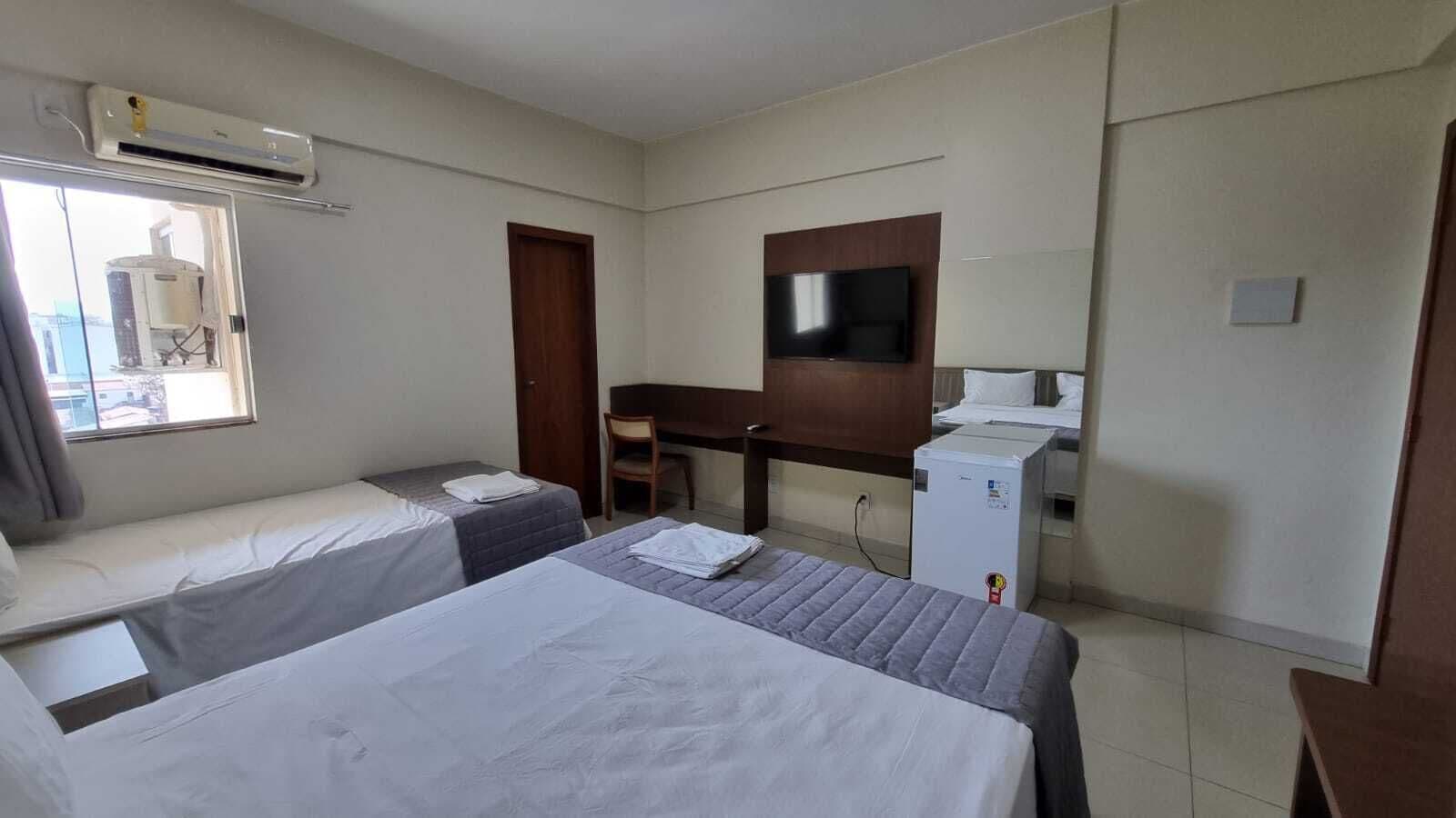 A hotel room with two beds, a desk, a TV, and a small refrigerator.