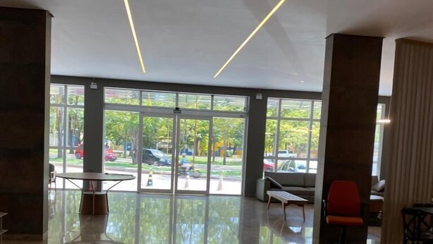 Un hall d  ’entrée spacieux avec un sol en marbre poli, de grandes fenêtres donnant sur la rue et un coin salon agrémenté d’un fauteuil rouge.