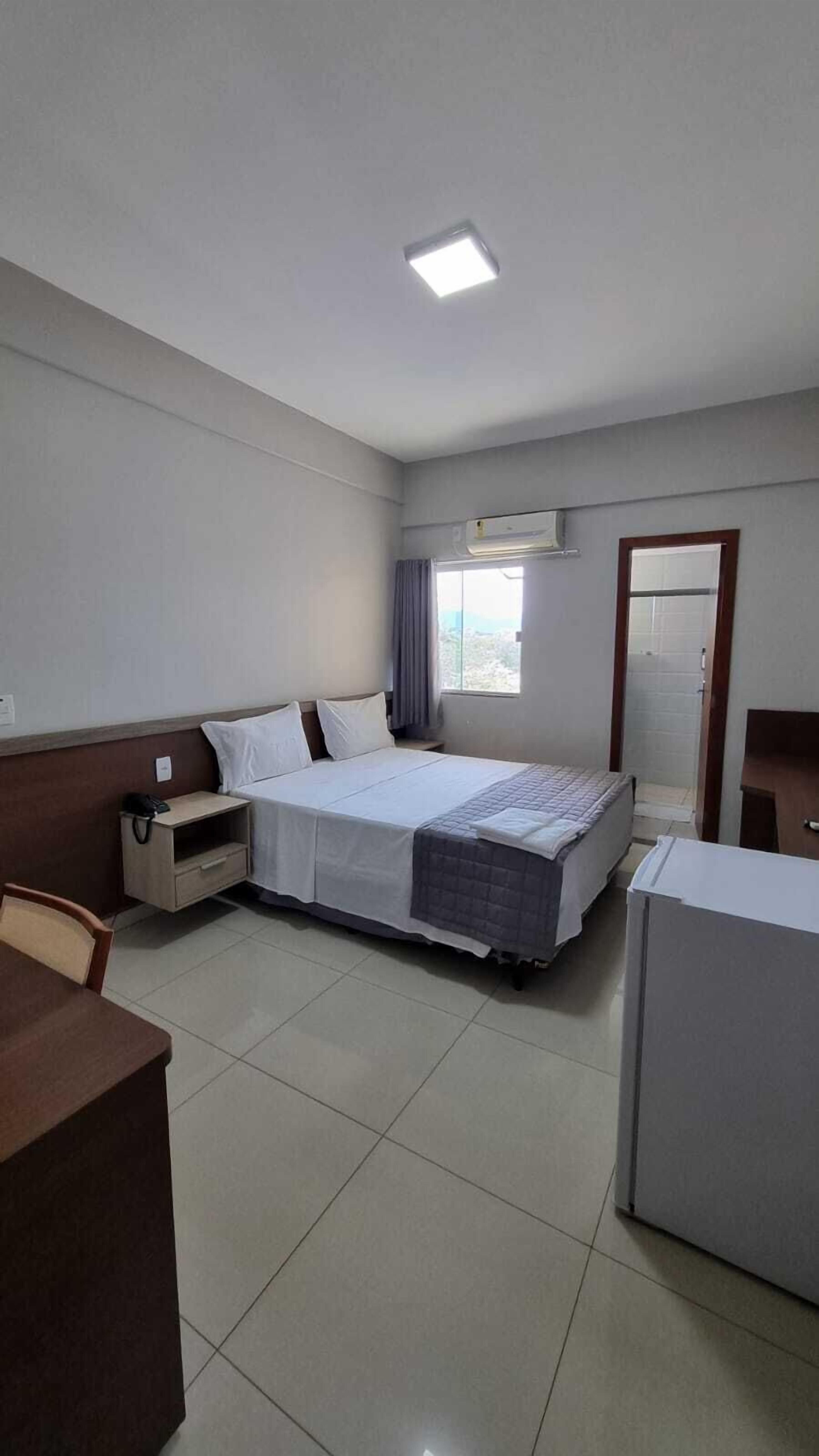 A hotel room with a bed, bedside table, chair, desk, and a window with curtains.