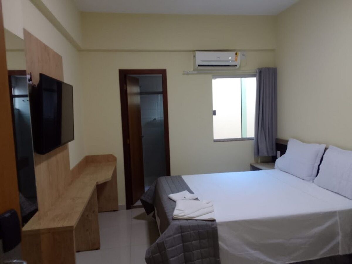 A hotel room with a bed, a desk, a television, and an air conditioning unit.