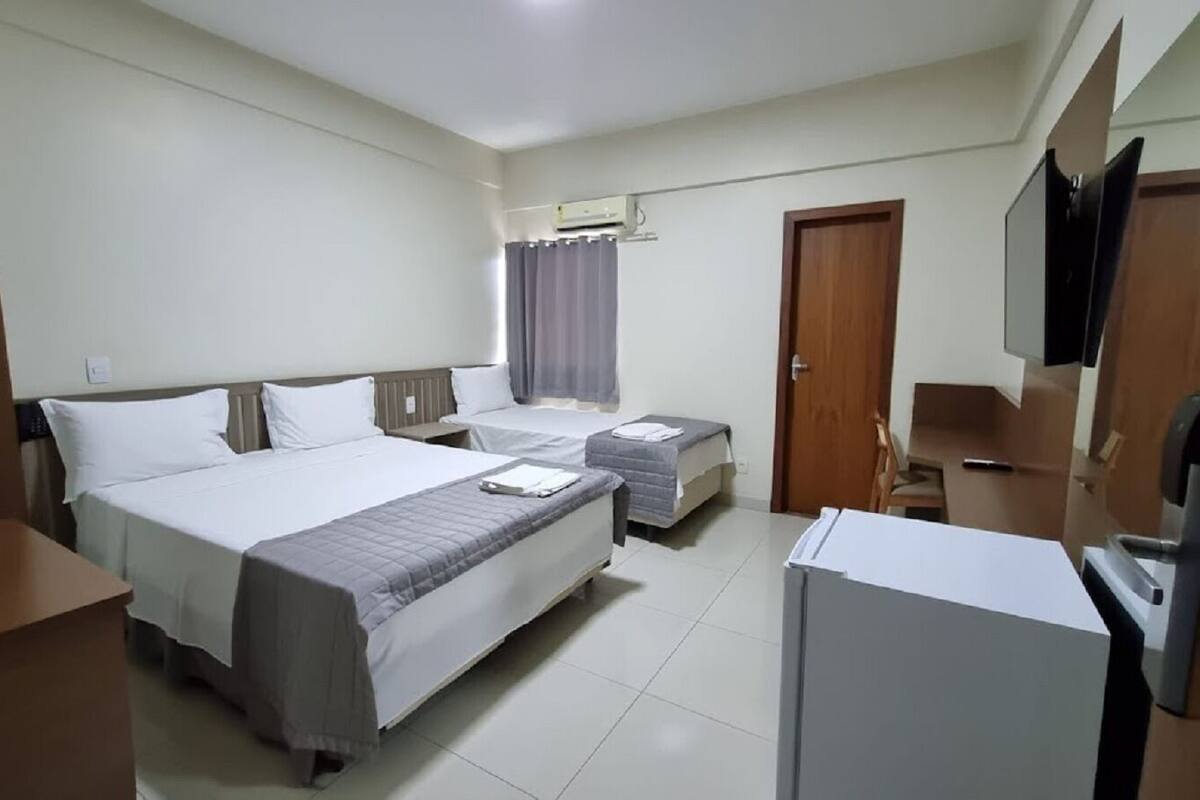 A hotel room with two beds, a desk, a chair, a TV, and a refrigerator.