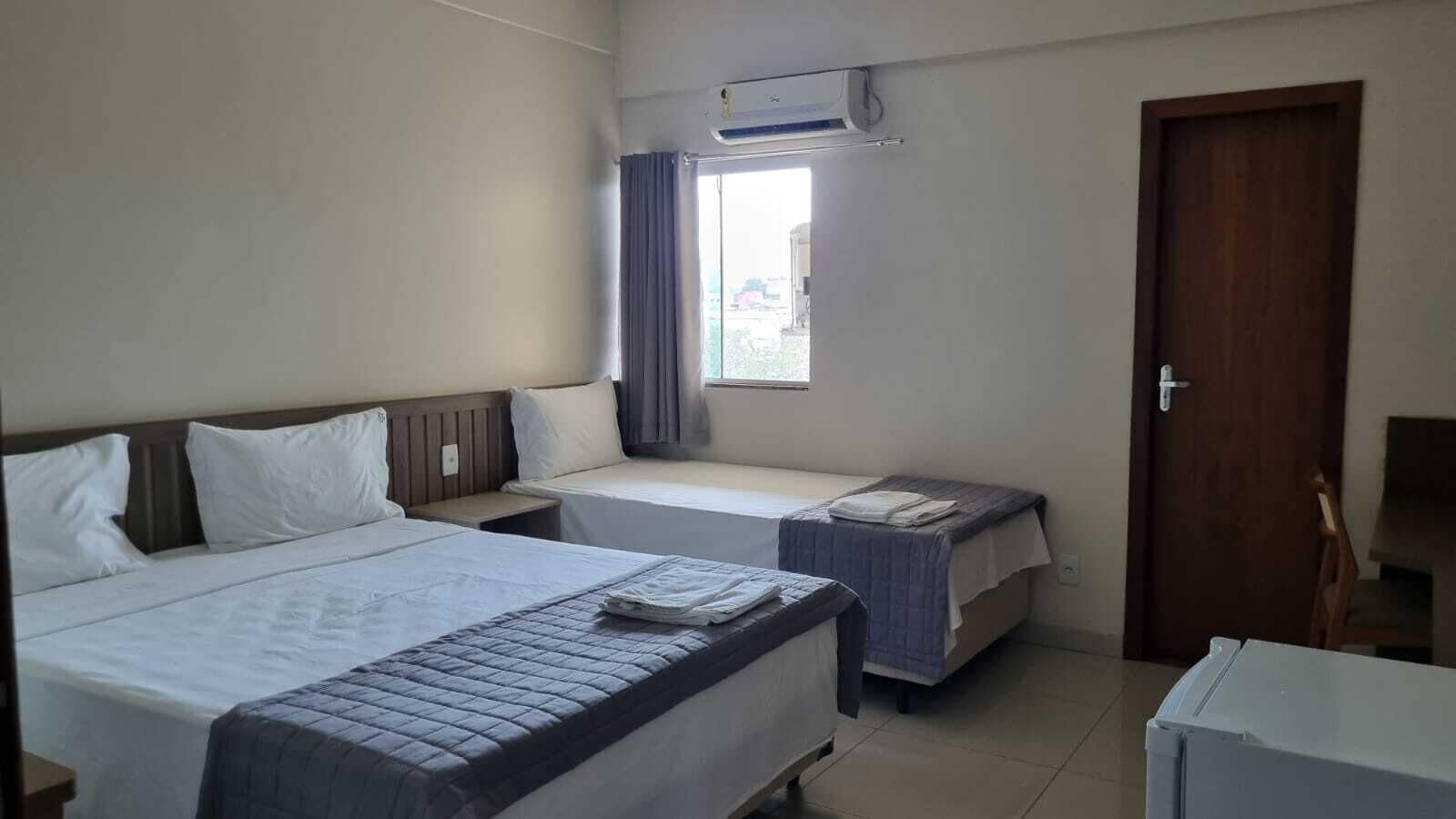 A hotel room with two beds, a window with curtains, a door, and a small table.