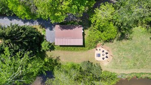 Luchtbeeld van een blokhut met een metalen dak, omringd door dichte groene bomen en een kleine open plek met terrasmeubilair.