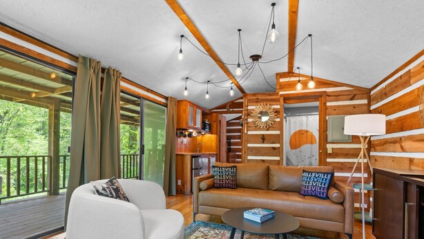 Een gezellig interieur van een chalet met een bank, fauteuil en een kleine tafel. Een houten trap leidt naar een vide.