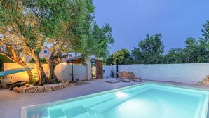 A swimming pool with lounge chairs, a hammock, and a stone wall.