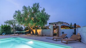 A pool area with lounge chairs, a pergola, and a stone structure.