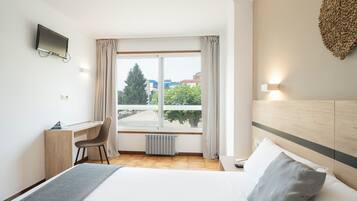 Habitación de hotel con cama, escritorio, silla, televisión y ventana con cortinas.