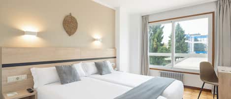 Habitación de hotel con dos camas, un escritorio, una silla, ventana con vistas y una lámpara fijada a la pared.