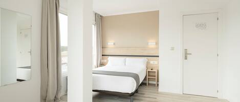 Una habitación de hotel con cama, mesita de noche y espejo.