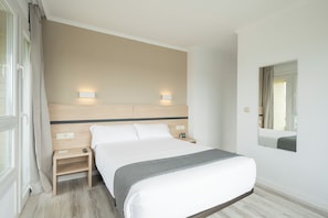 Una habitación de hotel con una cama grande, mesitas de noche, un espejo y una ventana con cortinas.