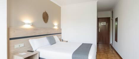 A hotel room with a bed, bedside table, and wall-mounted light fixture.