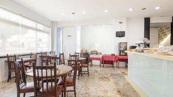 A dining area with wooden tables and chairs, a buffet counter, and a large window providing a view of the city.