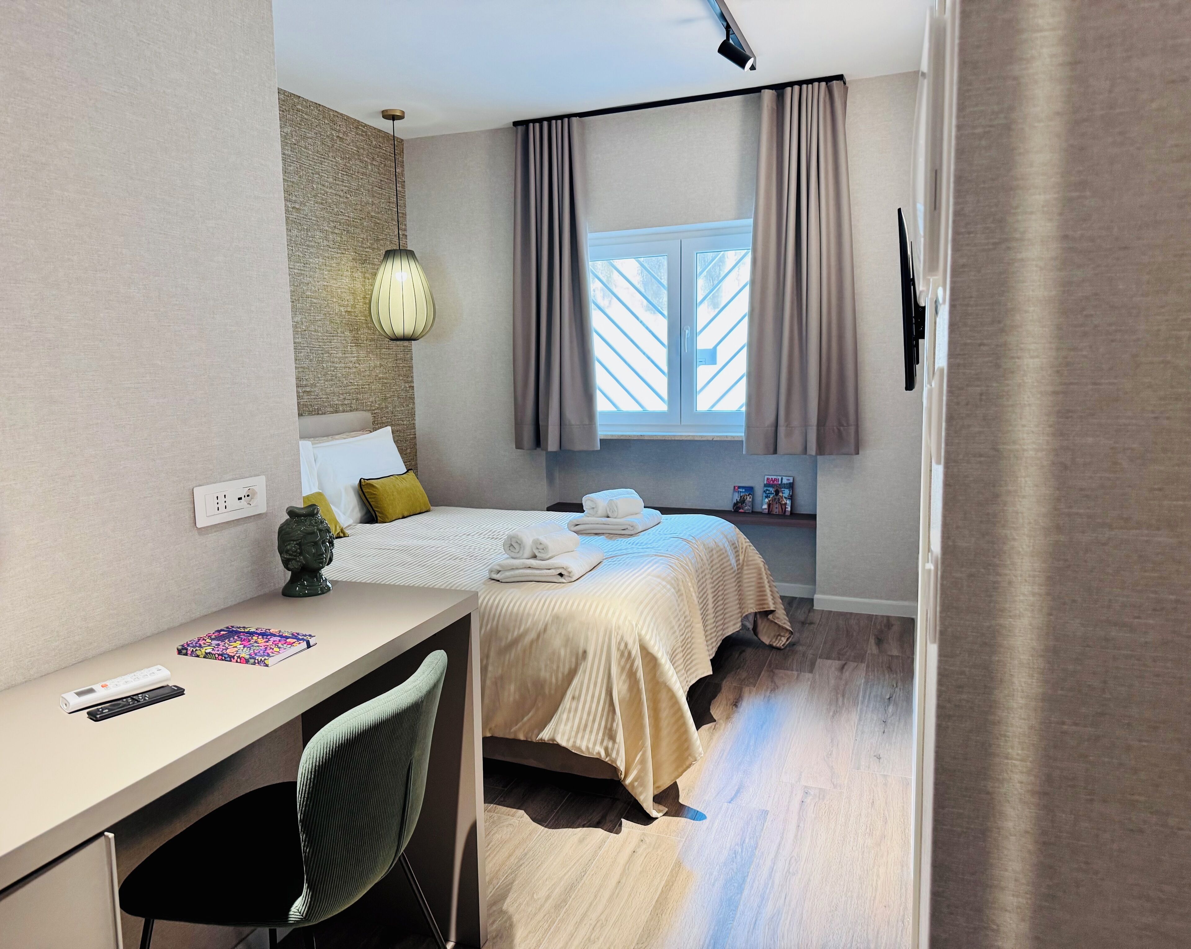 Una camera d'albergo moderna con un letto, un comodino, una lampada e una finestra con tende.
