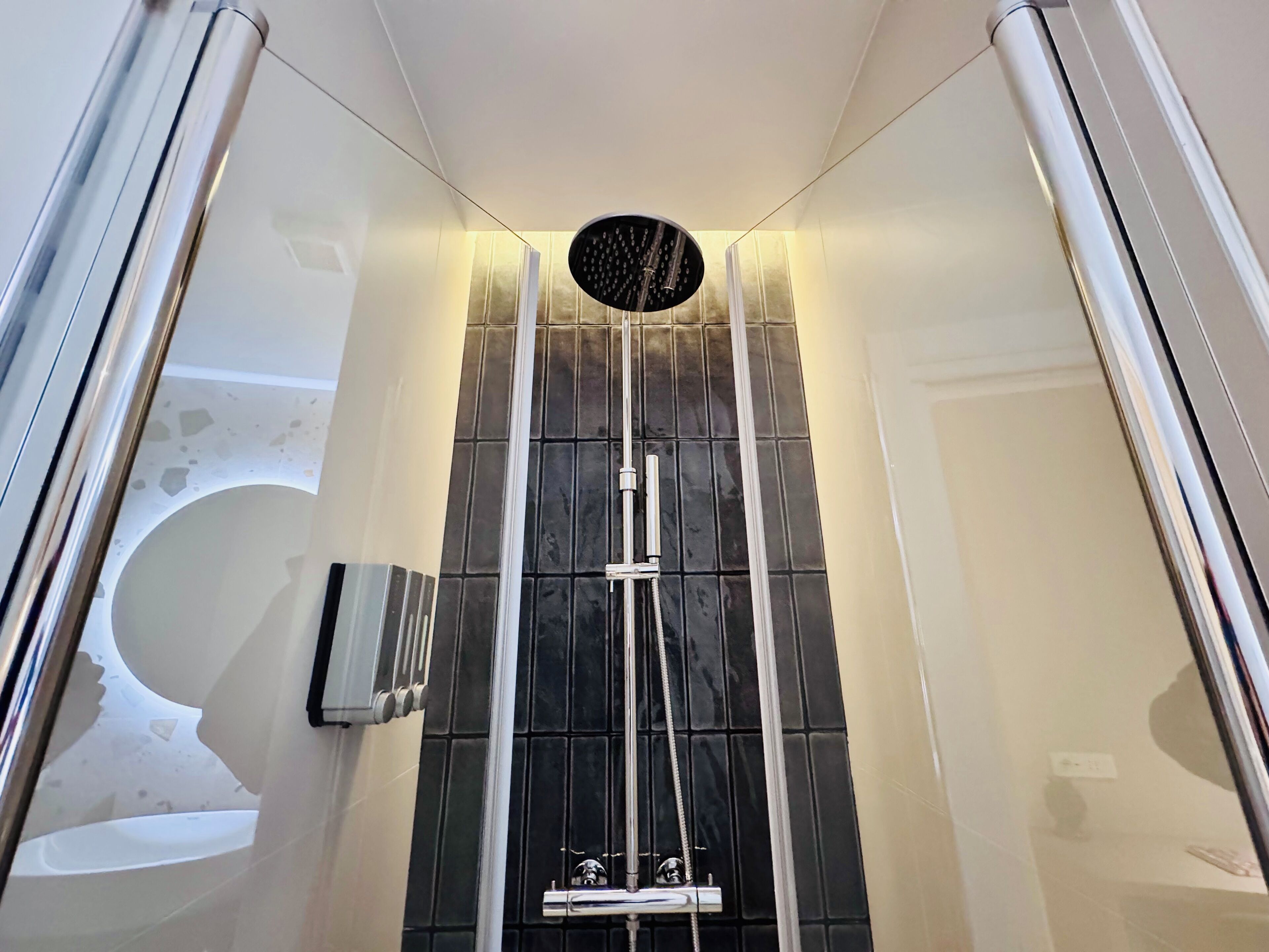 A modern shower with a rain showerhead, a handheld showerhead, and a handheld massager.