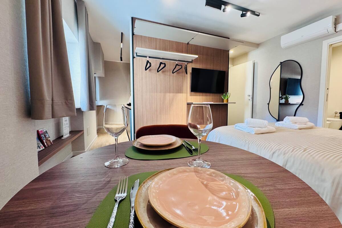 Habitación de hotel con zona de comedor, cama, televisión y espejo.