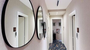 Ein Flur mit drei großen Spiegeln an der Wand, einer Deckenleuchte und einer Tür zu einem Raum mit Terrazzo-Boden.