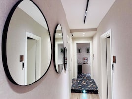 Un corridoio con tre grandi specchi a parete, una luce a soffitto e una porta che dà su una stanza con pavimento in terrazzo.