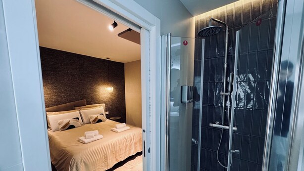 Ein modernes Hotelzimmer mit einem Bett, einer gläsernen Dusche und einer strukturierten Wand.