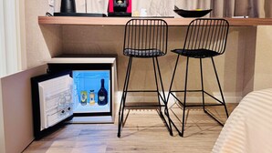 Ein kompaktes Hotelzimmer mit Küchenzeile, zwei schwarzen Stuhlen mit Drahtgestell, einer Kaffeemaschine und einem Minikühlschrank, gefüllt mit Getränken.