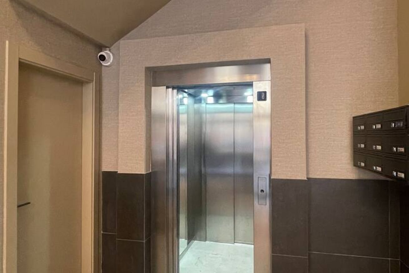 A modern elevator with a metallic finish, a wall-mounted mailbox, and a door leading to another room.