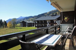 A balcony with a table and chairs overlooking a mountainous landscape with buildings.
