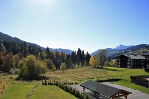 A mountainous landscape with a clear sky, a grassy field, and a building with a sloped roof.