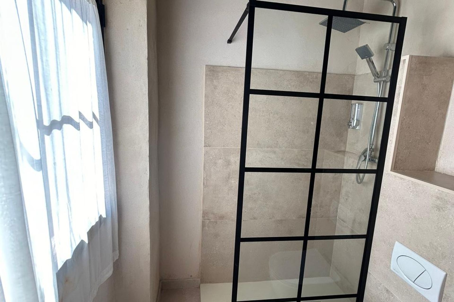 Una ducha con cerramiento de vidrio, diseño moderno, paredes con azulejos color beige y ducha visible.