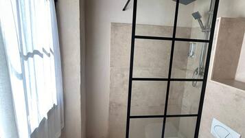 Una ducha con cerramiento de vidrio, diseño moderno, paredes con azulejos color beige y ducha visible.