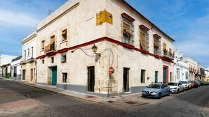 Un edificio histórico con fachada roja y blanca, múltiples ventanas y una calle frente a él con automóviles estacionados.