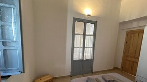 Un dormitorio con una cama, un cofre de madera, una puerta con luz encima y un armario de madera.