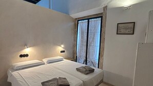 Un dormitorio con una cama, dos lámparas de pared, un ventanal con cortinas y un pequeño cuadro en la pared.