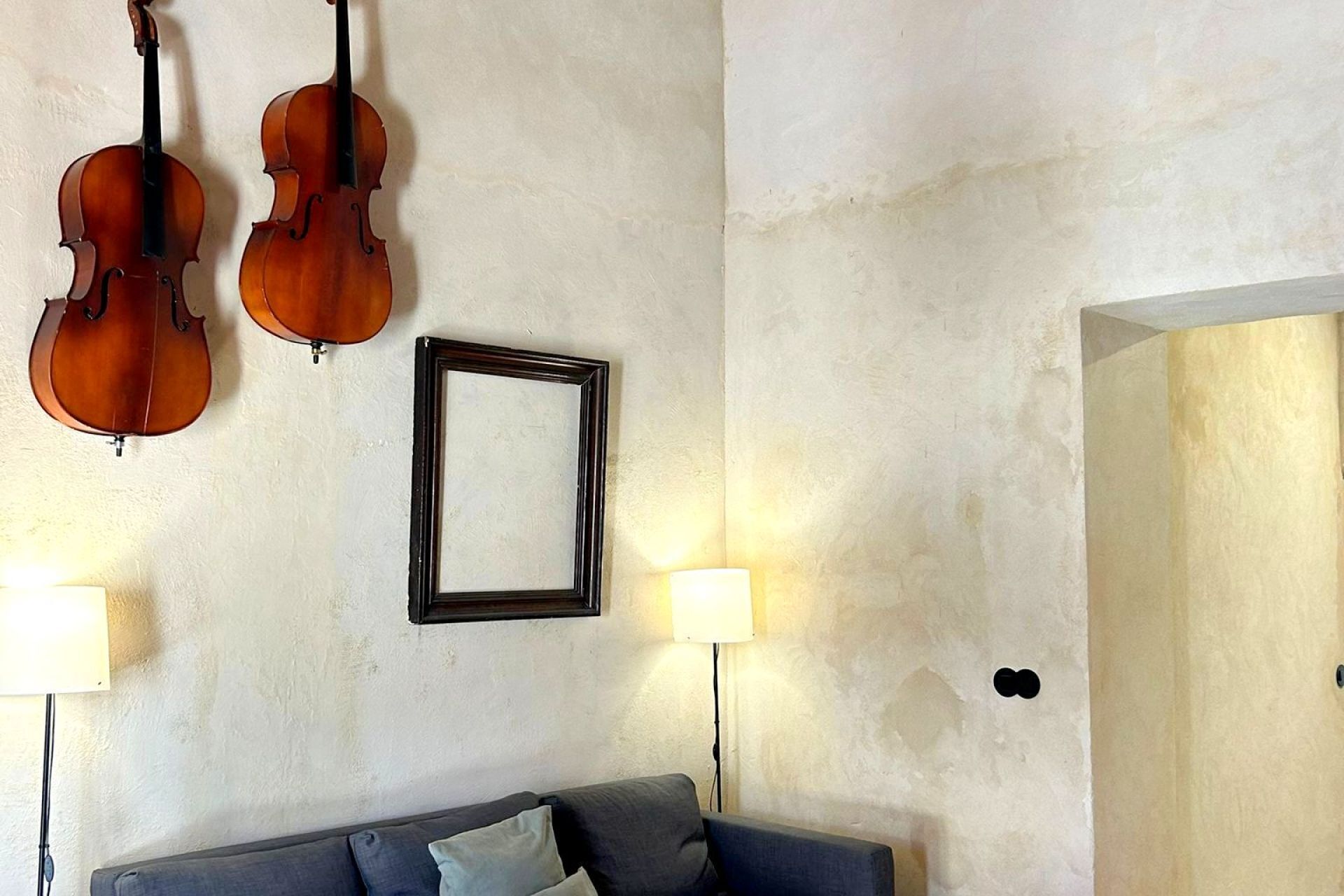Una habitación con dos violines colgados en la pared, un cuadro enmarcado y un sofá con dos lámparas.
