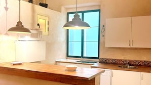 Een keuken met een houten aanrecht, witte kasten, een raam met blauwe luiken en hangende lampen.