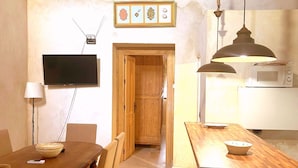 Een compacte keuken met een houten eettafel, een magnetron en een aan de muur bevestigde televisie.
