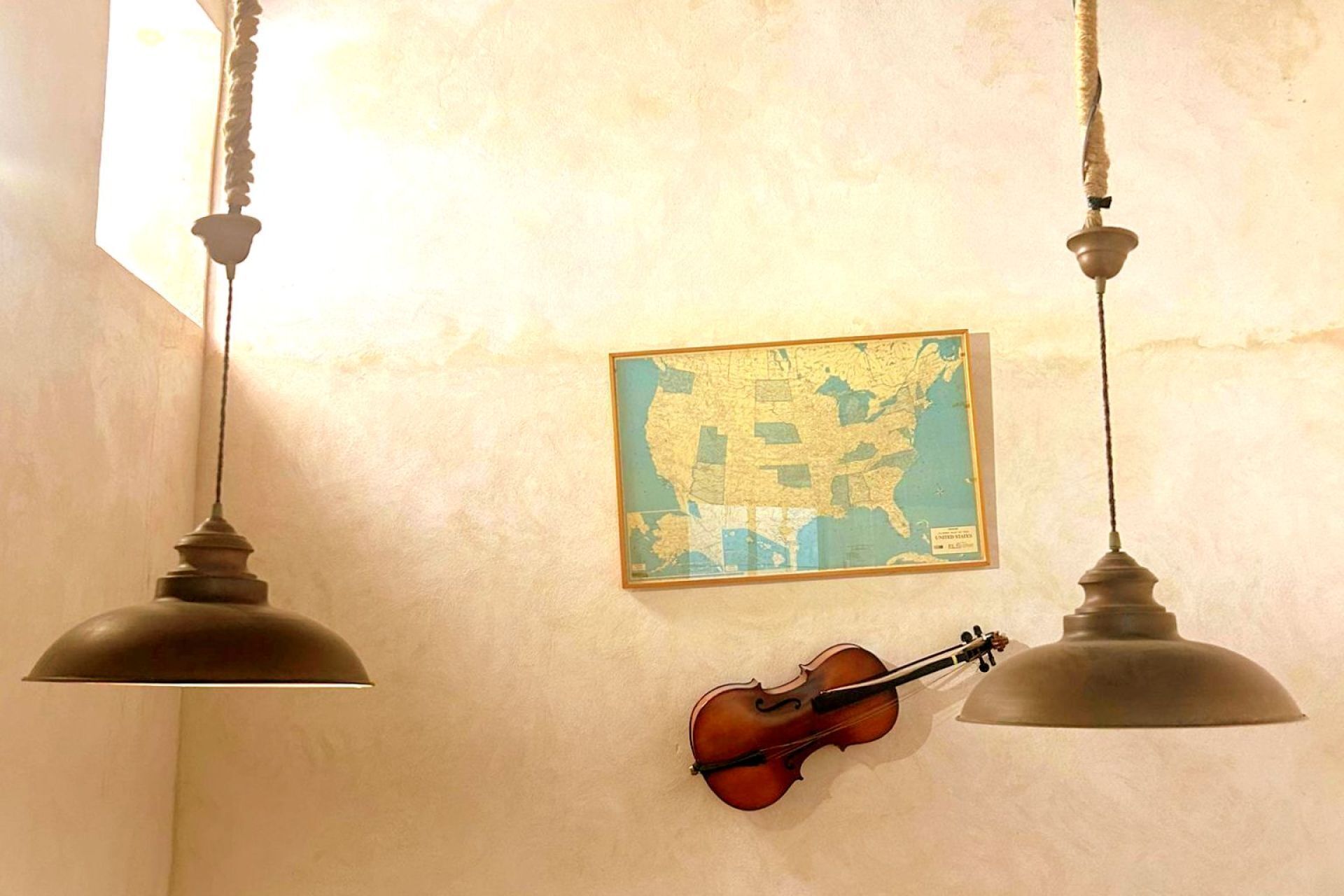 Une pièce avec deux lampes suspendues, une carte encadrée des États-Unis accrochée au mur et un violon appuyé contre le mur.
