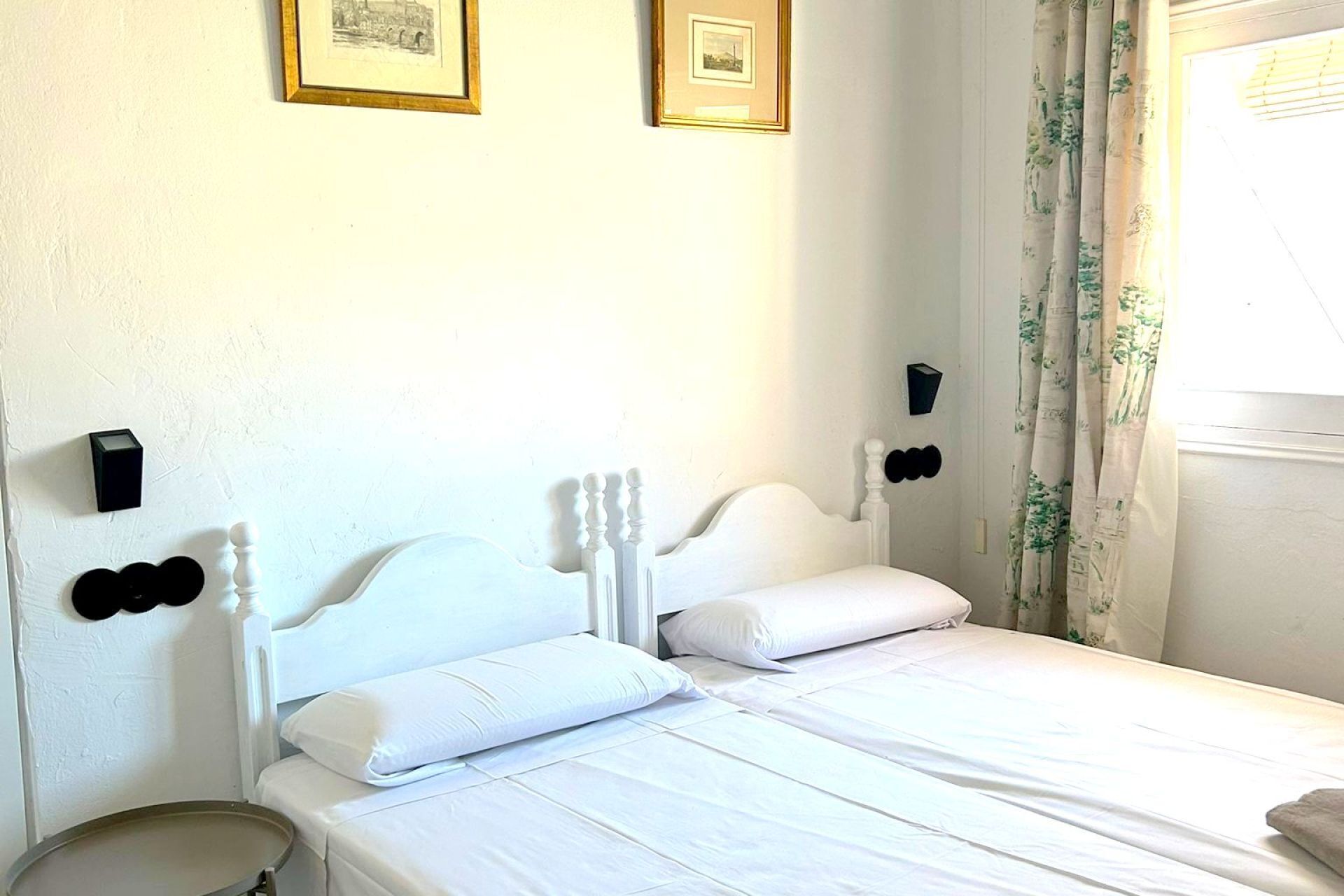 Un lit simple avec une tête de lit blanche et deux oreillers, une petite table de chevet et une lampe fixée au mur.