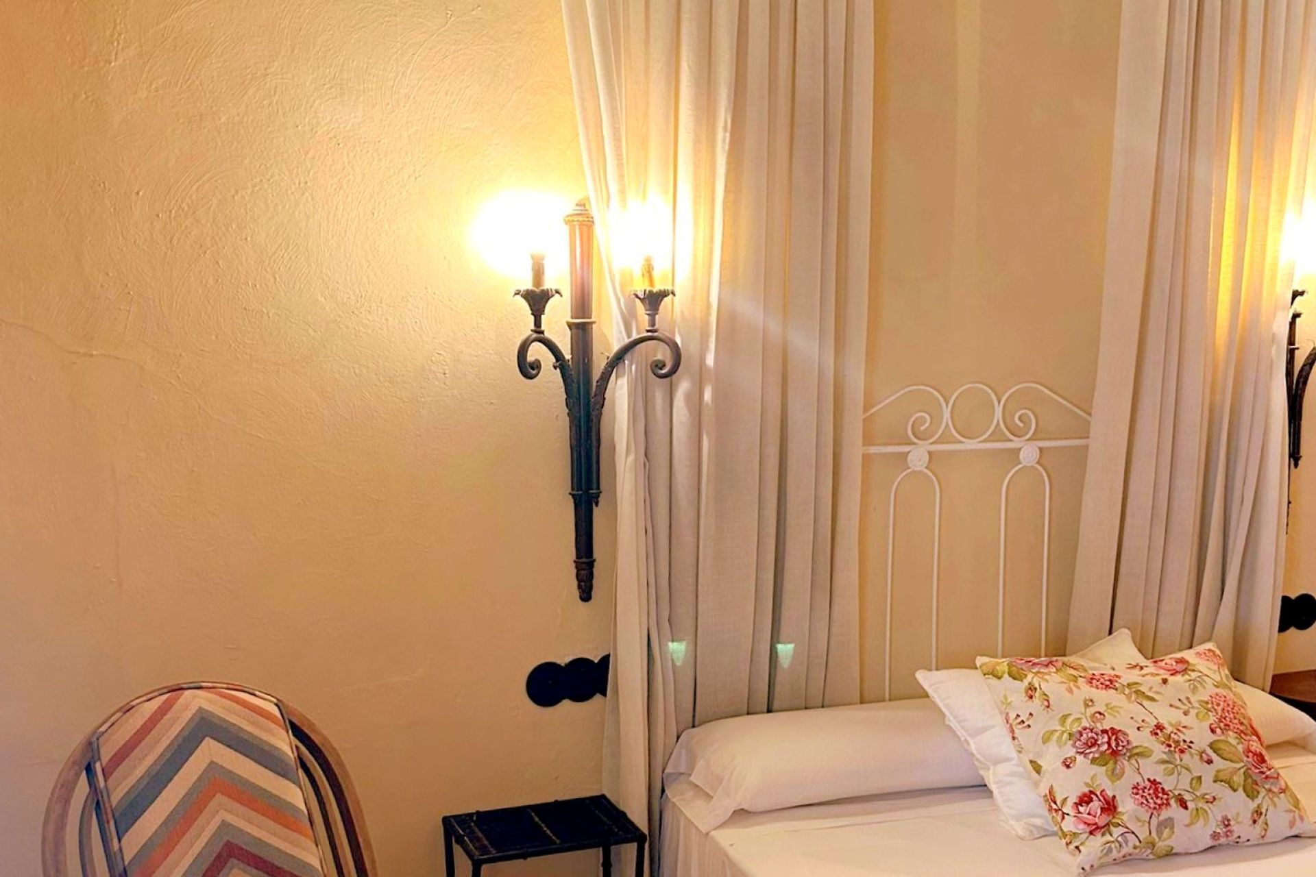 A bedroom with a bed, curtains, a wall-mounted light fixture, and a chair.