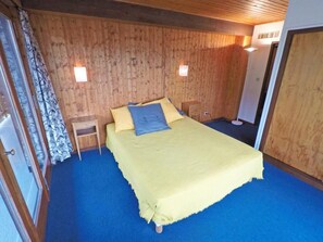 A bedroom with a wooden wall, a bed with a yellow bedspread, a small bedside table, and a nightstand. - 300m from resort center, 3rd floor, balcony, 70m², Les Gets (Les Gets)