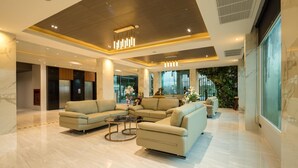 A spacious lobby with a sectional sofa, a coffee table, and a large window offering a view of greenery. - Benjaphorn Grandview Hotel (Songkhla)