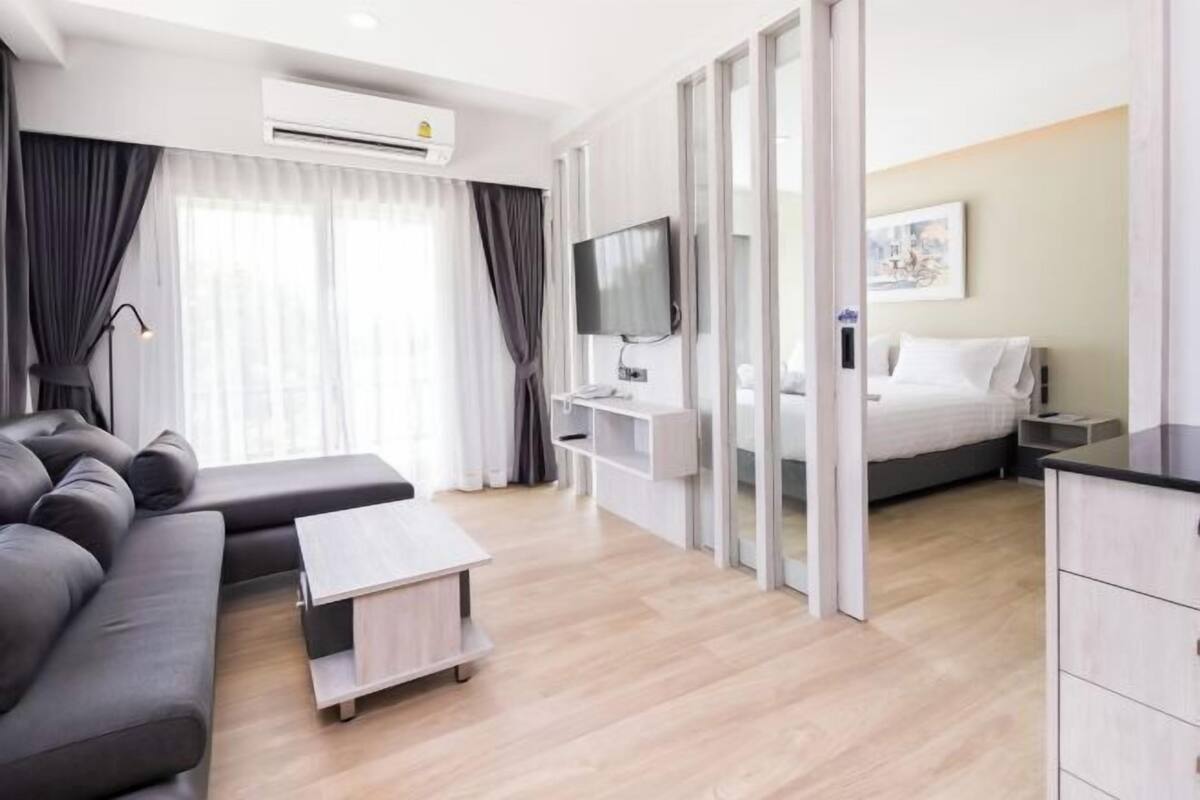 A modern hotel room with a sofa, a TV, a bed, and a desk.