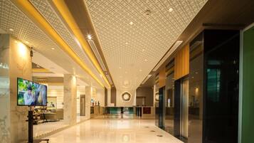 A spacious lobby with a high ceiling, a reception desk, and a television screen.