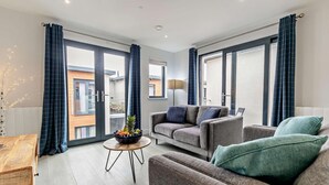 Ett modernt vardagsrum med en soffa, fåtöljer, ett soffbord och utsikt genom stora glasdörrar.