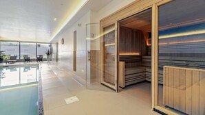 Ett modernt inomhuspoolområde med en glasvägg, en bastu och en sittgrupp med utsikt över poolen.