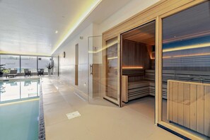 A modern indoor pool area with a glass enclosure, a sauna, and a seating area with a view of the pool.