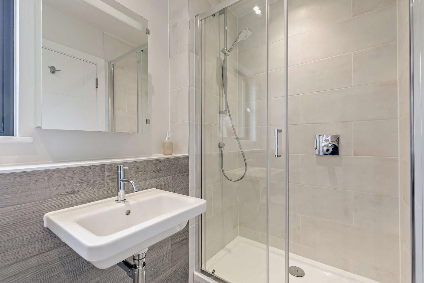 A modern bathroom with a glass-enclosed shower, a white sink, and a mirror above it.